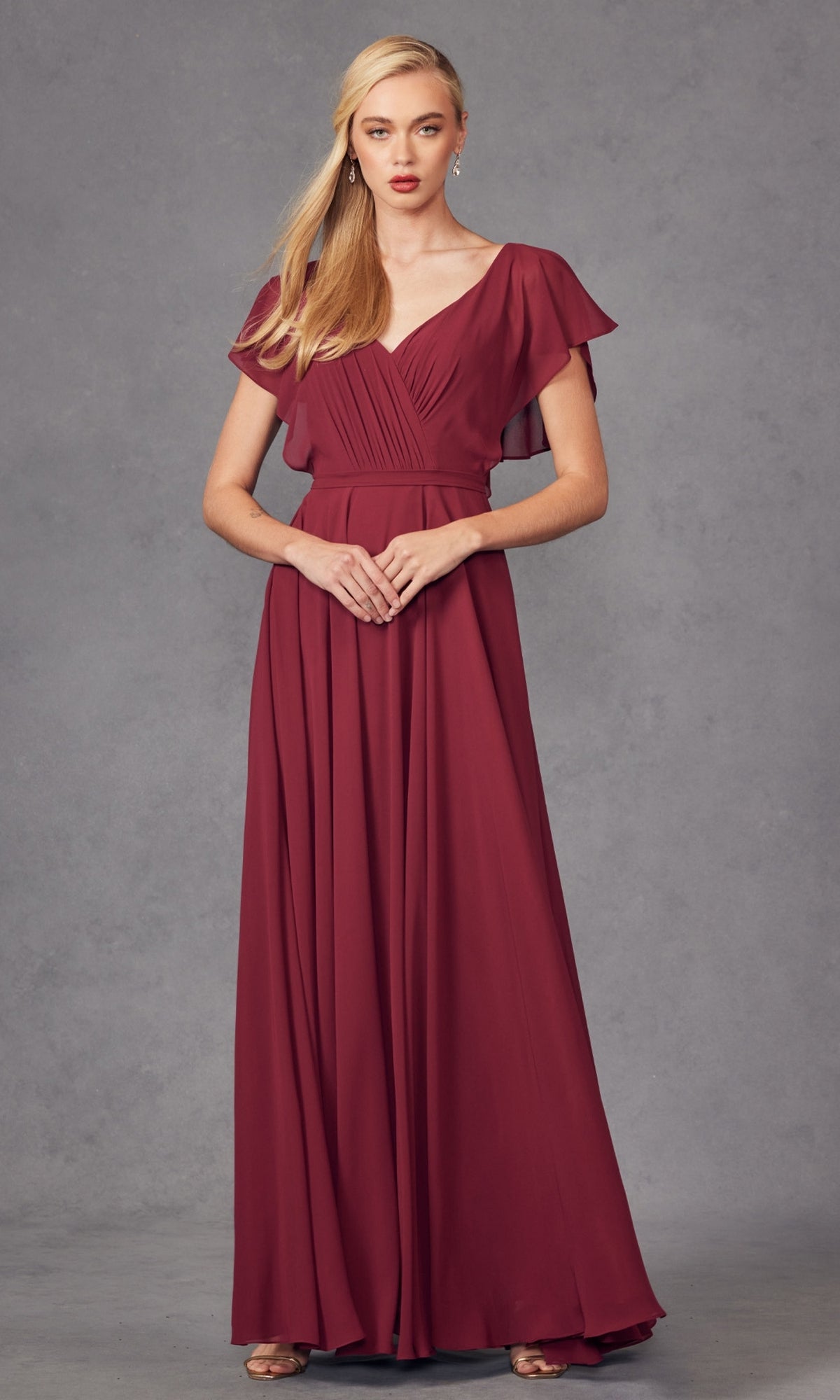 A woman wears the Flutter-Sleeve Long Formal Evening Gown 261—a floor-length, short-sleeve burgundy A-line dress with a V-neck and gathered waist—posing against a plain gray background.