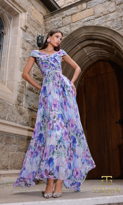A woman stands on stone steps before an arched wooden door, wearing the Terani 261C6641 long formal dress in blue purple. She pairs it with silver shoes. The image displays the Terani logo in the bottom right corner.