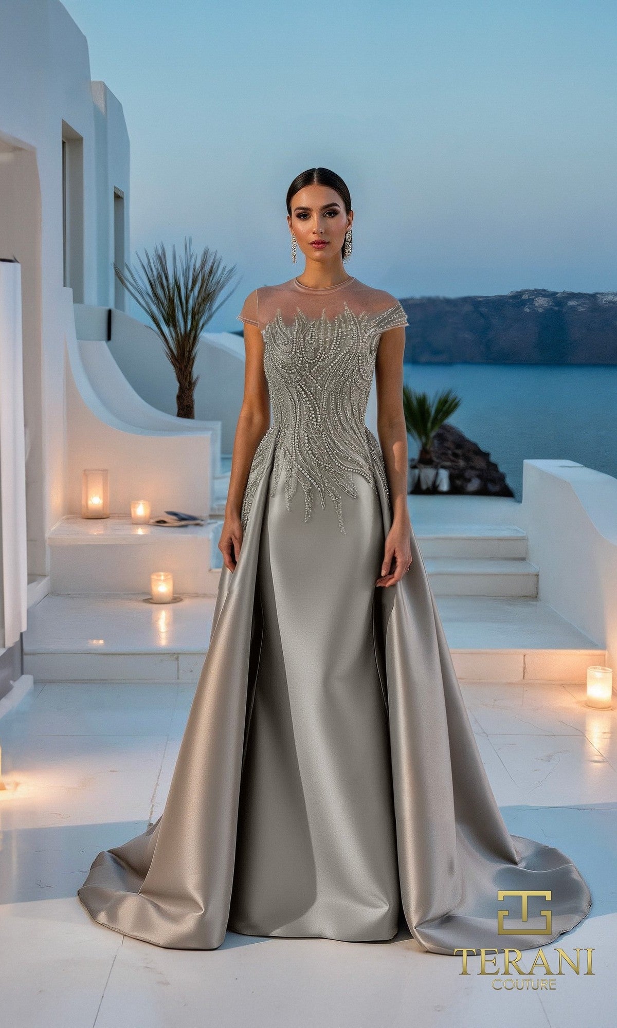 A woman in a floor-length, taupe modest long formal dress (Terani 261E6254) stands on a white terrace overlooking the sea at sunset. Intricate beading adds elegance to her look.