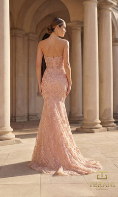 A woman in the Terani 261GL6001 Long Formal Dress stands with her back to the camera, blush pink sequins shimmering on the strapless beaded gown in a columned outdoor setting.
