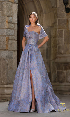 A woman in a Blue Rose long formal dress (Terani 261M6453) with a jeweled brooch and front slit stands gracefully before a stone archway.