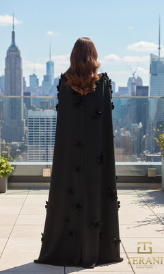 A woman with wavy brown hair stands on a rooftop, facing away, wearing the Long Formal Dress: Terani 261M6687. The city skyline, with the Empire State Building in view, stretches out behind her.