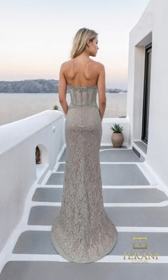 A woman in the Terani 261P6118 long formal dress stands on a minimally decorated outdoor terrace, facing away with a view of the sea.