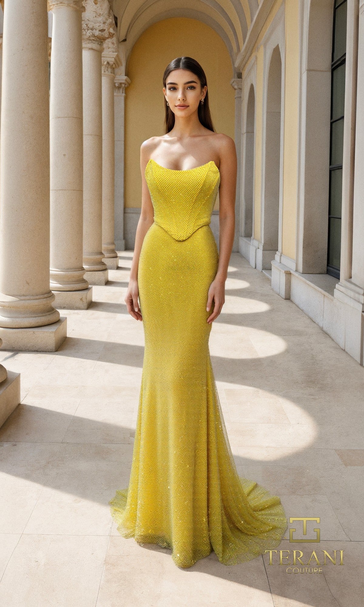 A woman stands in a sunlit colonnade wearing the Long Formal Dress: Terani 261P6187?a strapless, floor-length yellow gown with a fitted bodice and slight train. The 