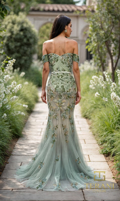 A woman wearing the Terani 261P6676 long formal dress, an off-the-shoulder light green gown with 3D floral appliques, stands on a stone path in a garden, facing away from the camera.