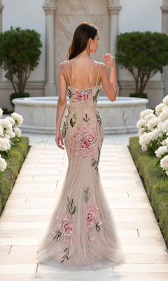 A woman in a fitted Terani 261P6677 long formal dress with floral embroidery walks down a stone path lined with white flowers and greenery, her back to the camera.