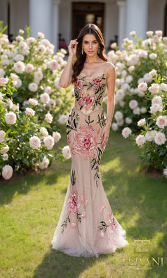 A woman wearing the Long Formal Dress Terani 261P6677 in Blush Multi stands on grass among blooming roses, with a building in the background.