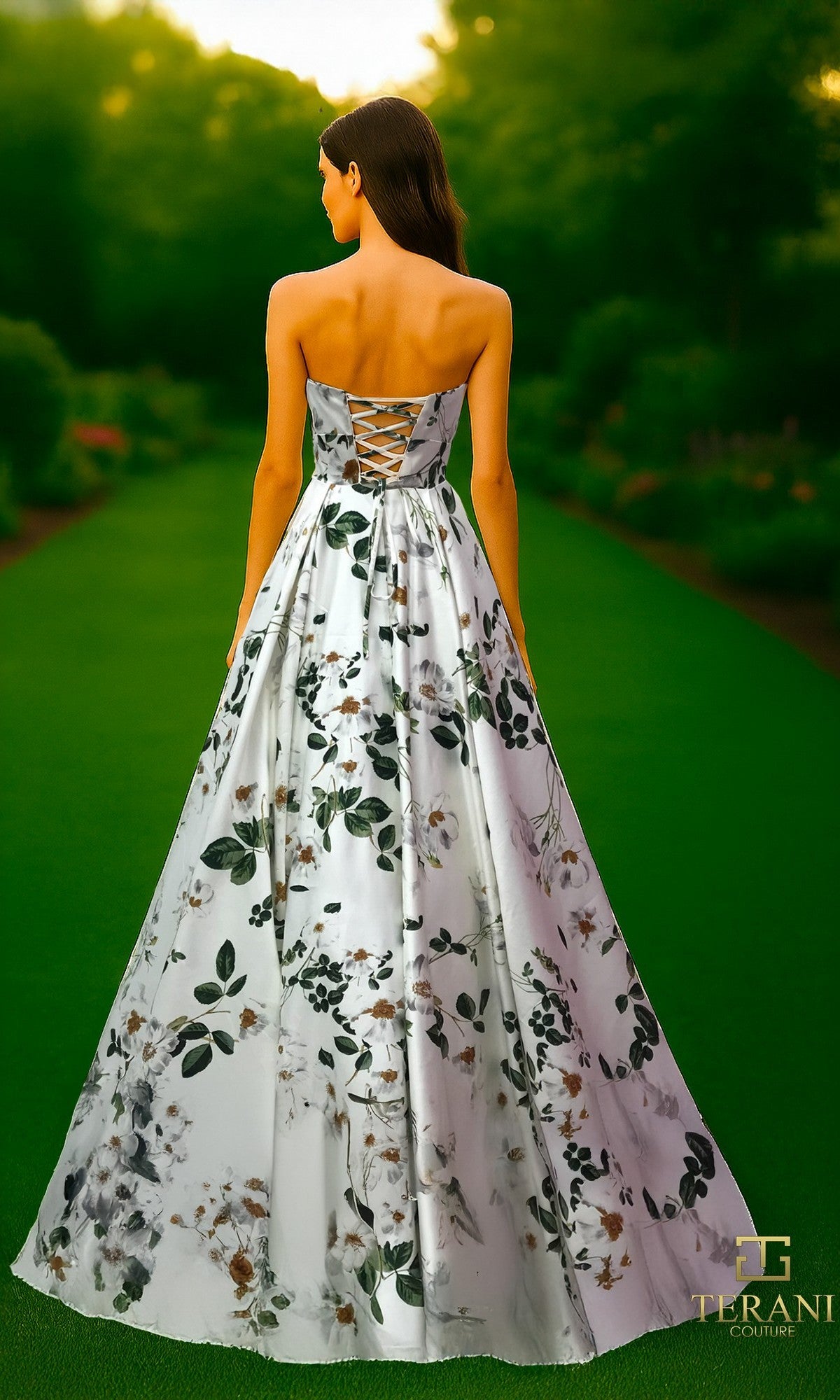 A woman stands outdoors wearing the Long Formal Dress: Terani 261P6705, which features a strapless neckline, floral-printed satin fabric, a lace-up back, and an elegant A-line skirt.