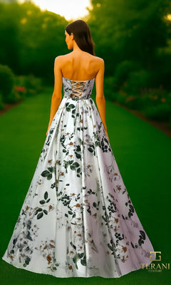 A woman stands outdoors wearing the Long Formal Dress: Terani 261P6705, which features a strapless neckline, floral-printed satin fabric, a lace-up back, and an elegant A-line skirt.