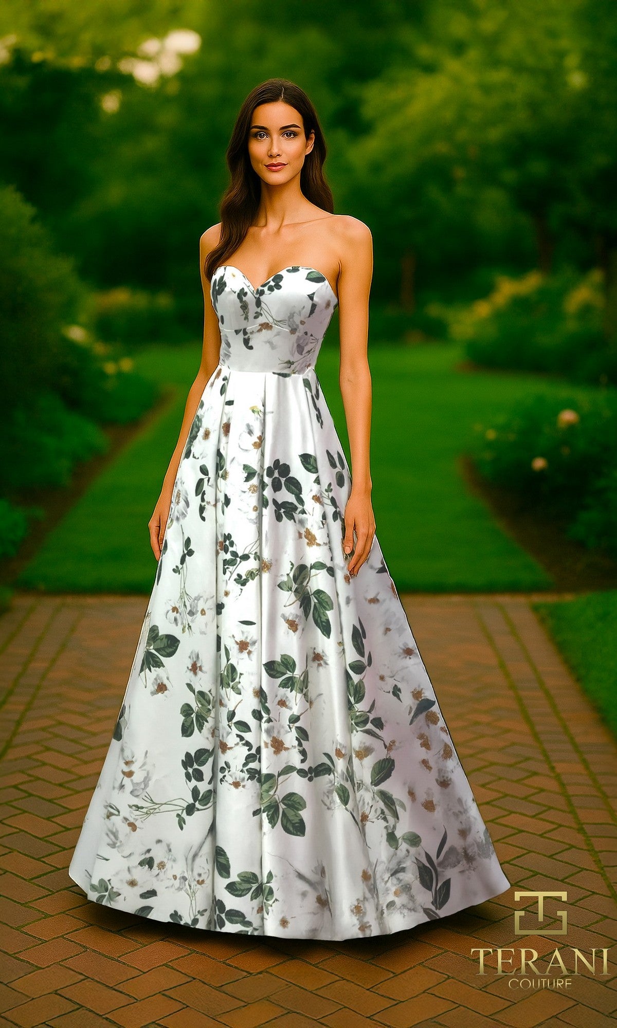 A woman stands outdoors in a strapless Terani 261P6705 long formal dress with an A-line skirt. The green and grey floral satin gown flows to the floor, set against lush greenery and a paved garden path.