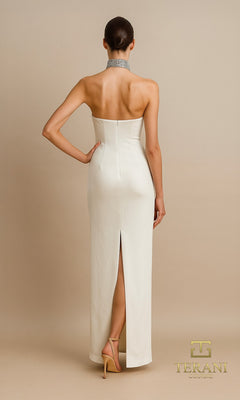 A woman faces away in the Long Formal Dress: Terani 261E6119, a strapless formal gown with a high back slit, accessorized with a silver choker and nude heels. The beige background displays the Terani Couture logo in the corner.