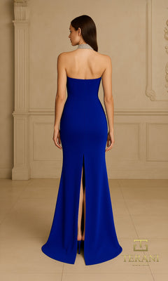 A woman stands indoors, facing away, wearing the Terani 261E6119?an elegant, strapless, floor-length royal blue formal dress with a back slit and silver choker.