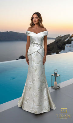 A woman in a mermaid silhouette, sage gold Terani 261E6252 long formal dress stands by a pool at sunset, overlooking the coast. A lantern is beside her and the Terani Couture logo is visible.