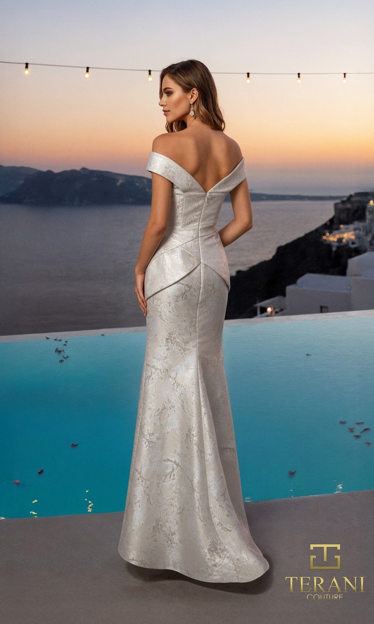 A woman in the Terani 261E6252 long formal dress with a mermaid silhouette stands by an infinity pool at sunset, gazing out over the sea and distant cliffs.