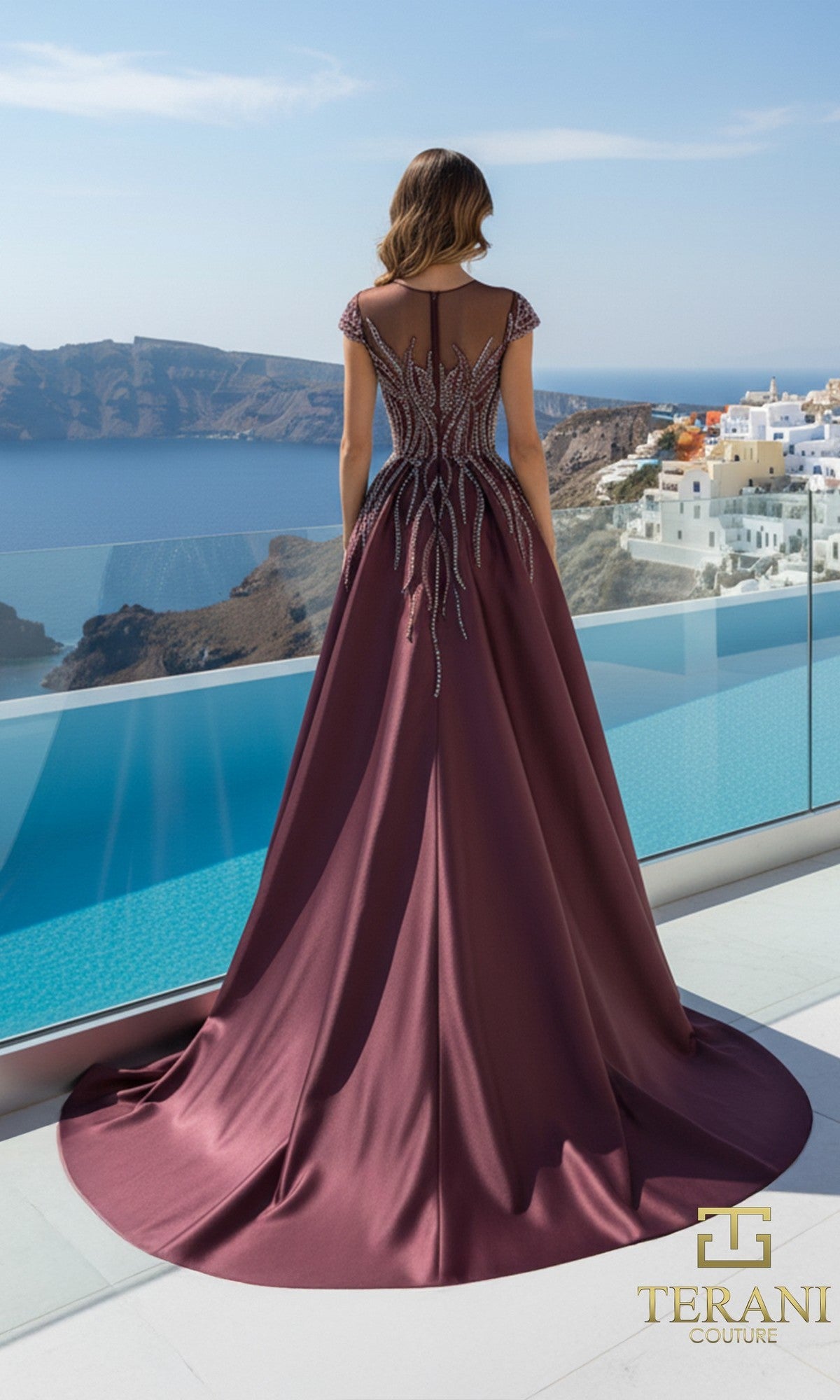 A woman in the Terani 261E6254 long formal dress, featuring beaded details and crafted from stretch Mikado, stands on a terrace overlooking the sea and white buildings, with the 