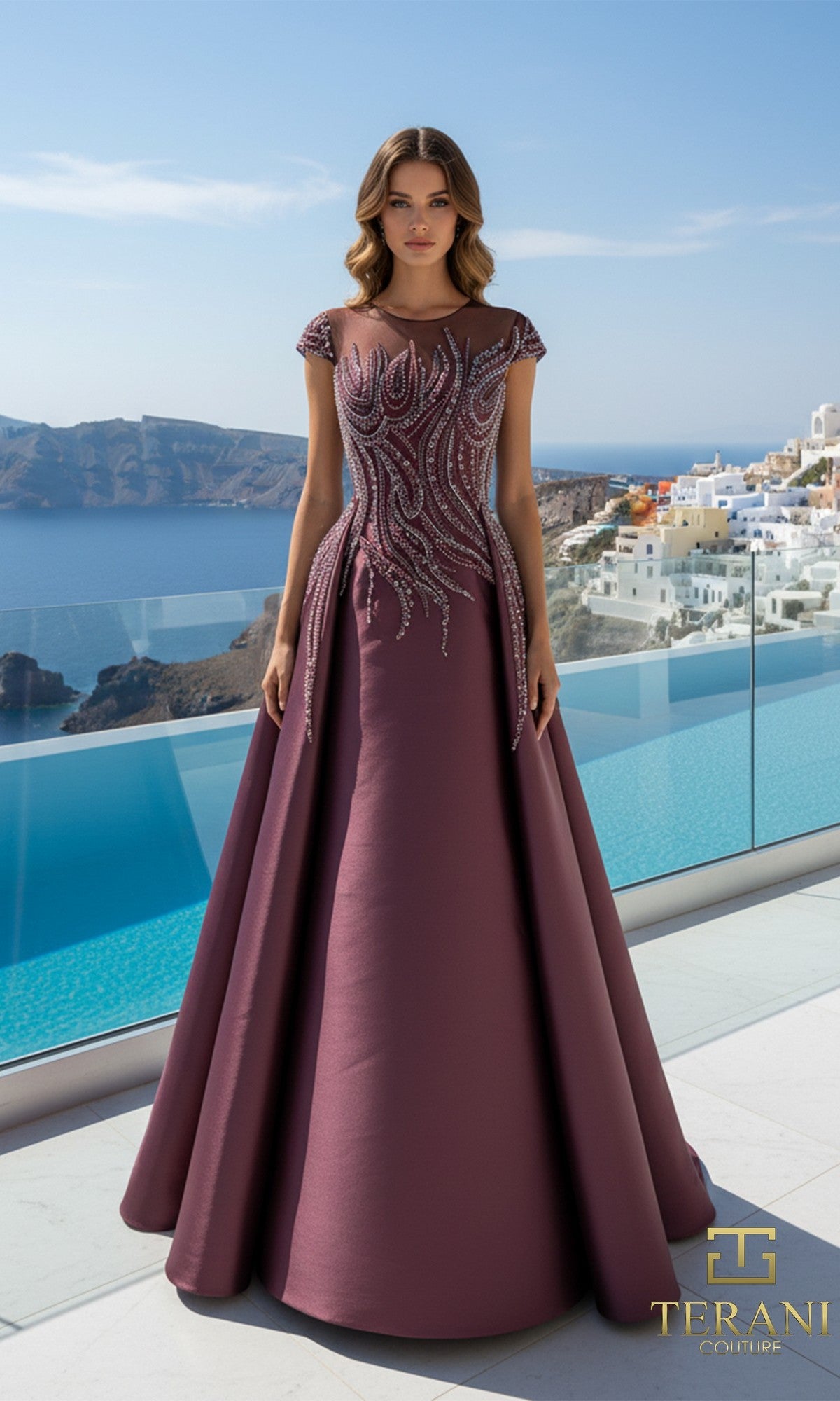 A woman in a wine Terani 261E6254 long formal dress stands on a terrace overlooking a pool and white hillside buildings.