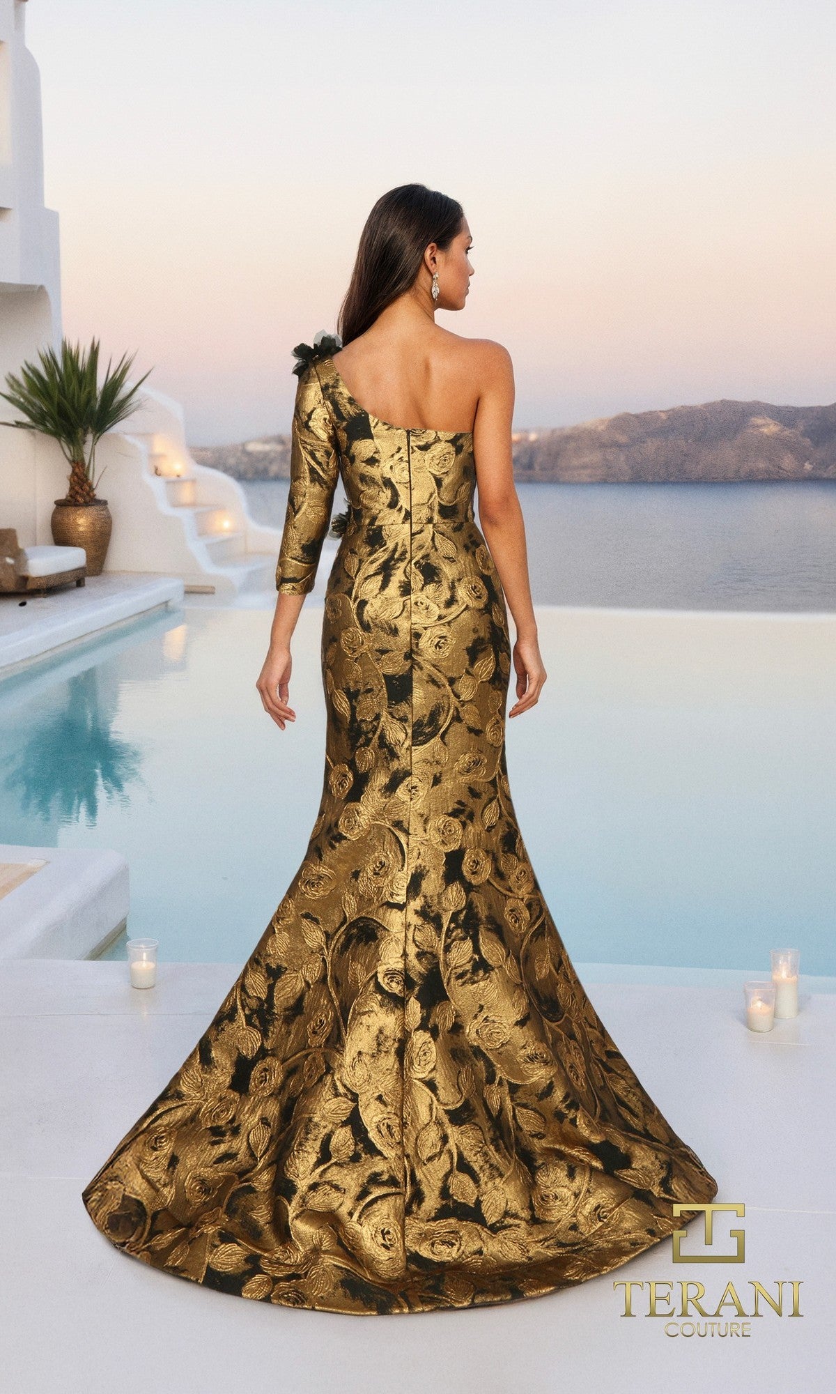 A woman wearing the Terani 261E6275 long formal dress with gold and black floral accents stands by a pool, overlooking a scenic sunset view.