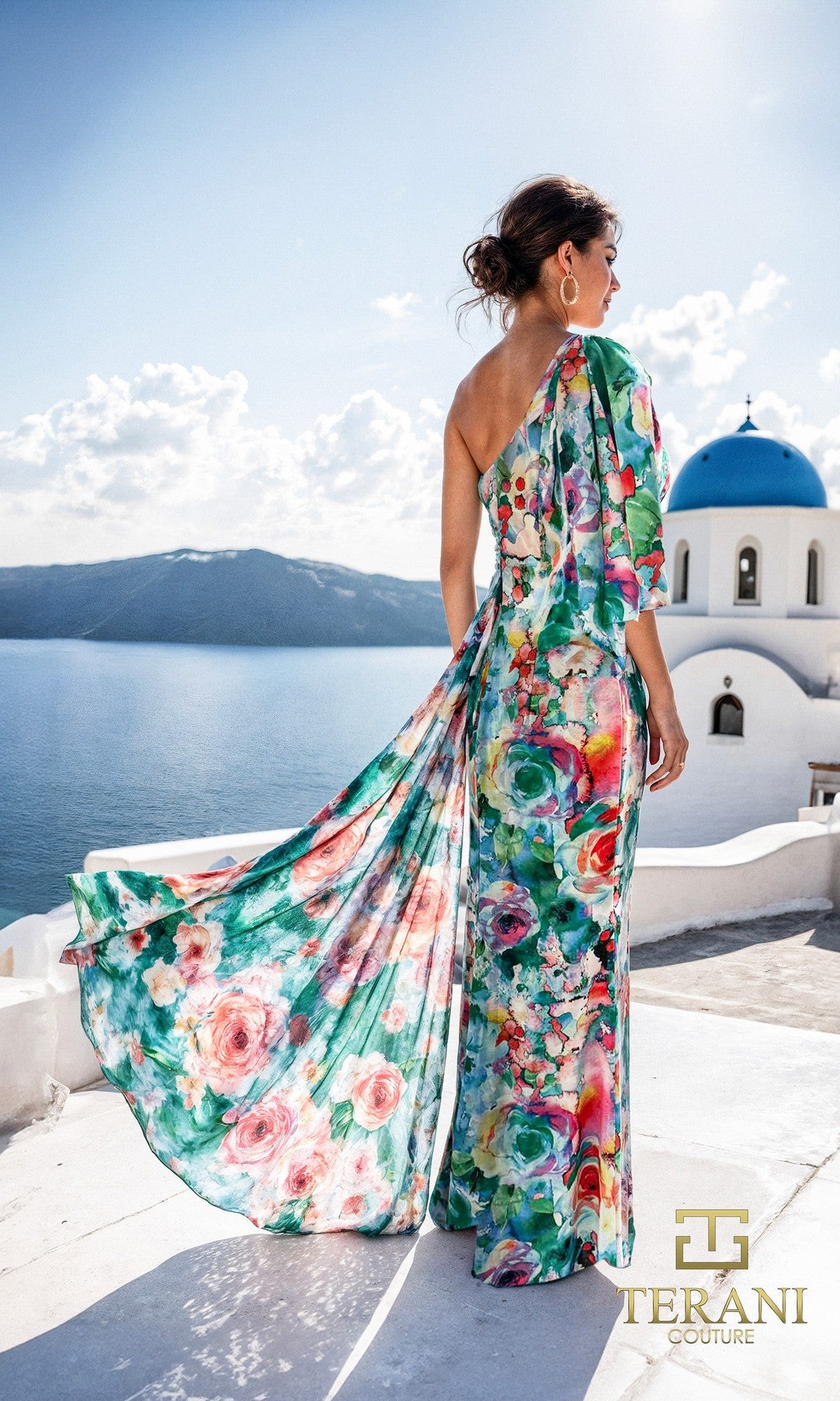A woman in the Terani 261E6646 Long Formal Dress stands on a white terrace overlooking the sea, with blue domed buildings in the background; the Terani Couture logo is visible.