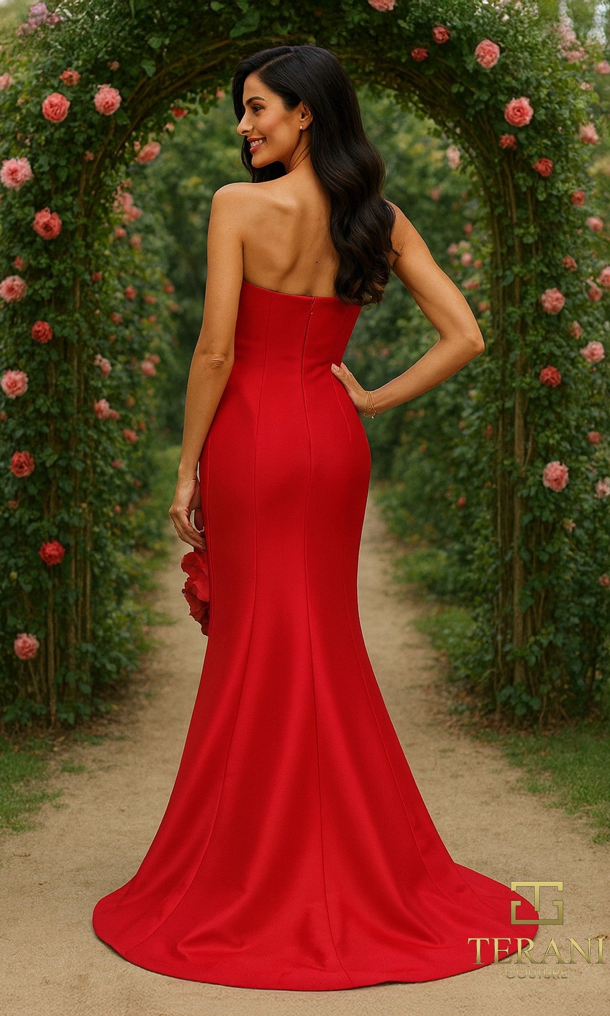 A woman wearing the Terani 261E6698 long formal dress stands outside on a garden path, surrounded by flowering arches and lush greenery.