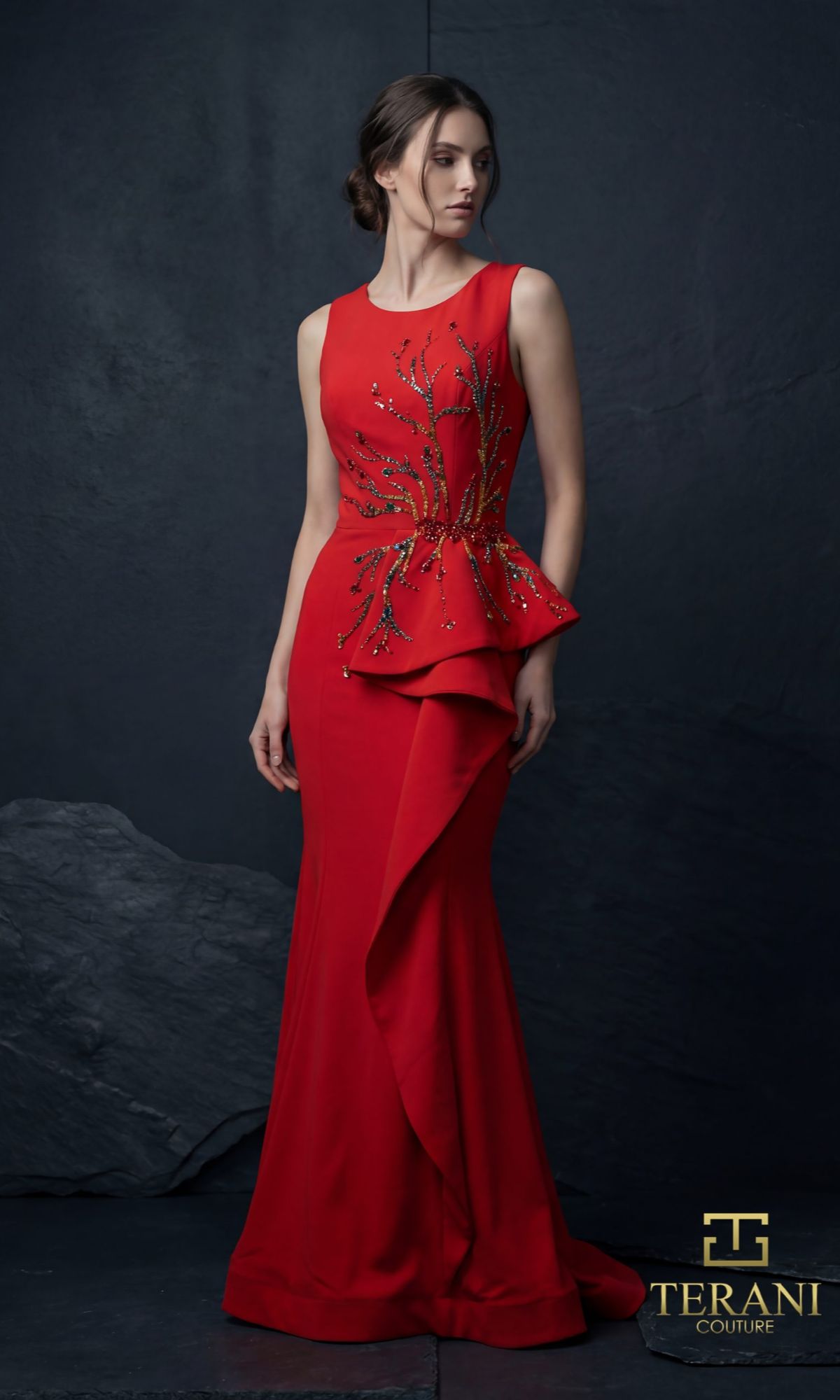 A woman wears the red Terani 261E6750 long formal dress with gold embellishments and peplum detail, standing against a dark textured backdrop. The Terani Couture logo appears in the bottom right corner.