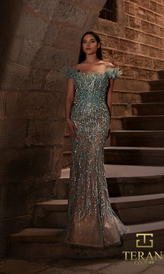 A woman in a detailed, off-the-shoulder sage nude Terani 261GL6373 long formal dress stands on stone steps before a brick wall. The Terani Couture logo appears in the lower right corner.