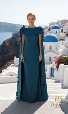 A woman in a dark green crepe Terani 261M6687 long formal dress with cape stands on a white-washed terrace overlooking blue-domed buildings and sea, with the "TERANI COUTURE" logo in the corner.