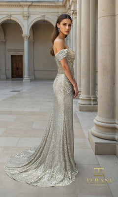 A woman in the Terani 261P6106 long formal dress stands gracefully in a marble courtyard, her off-the-shoulder floor-length silver sequin gown shimmering elegantly among columns and arches.