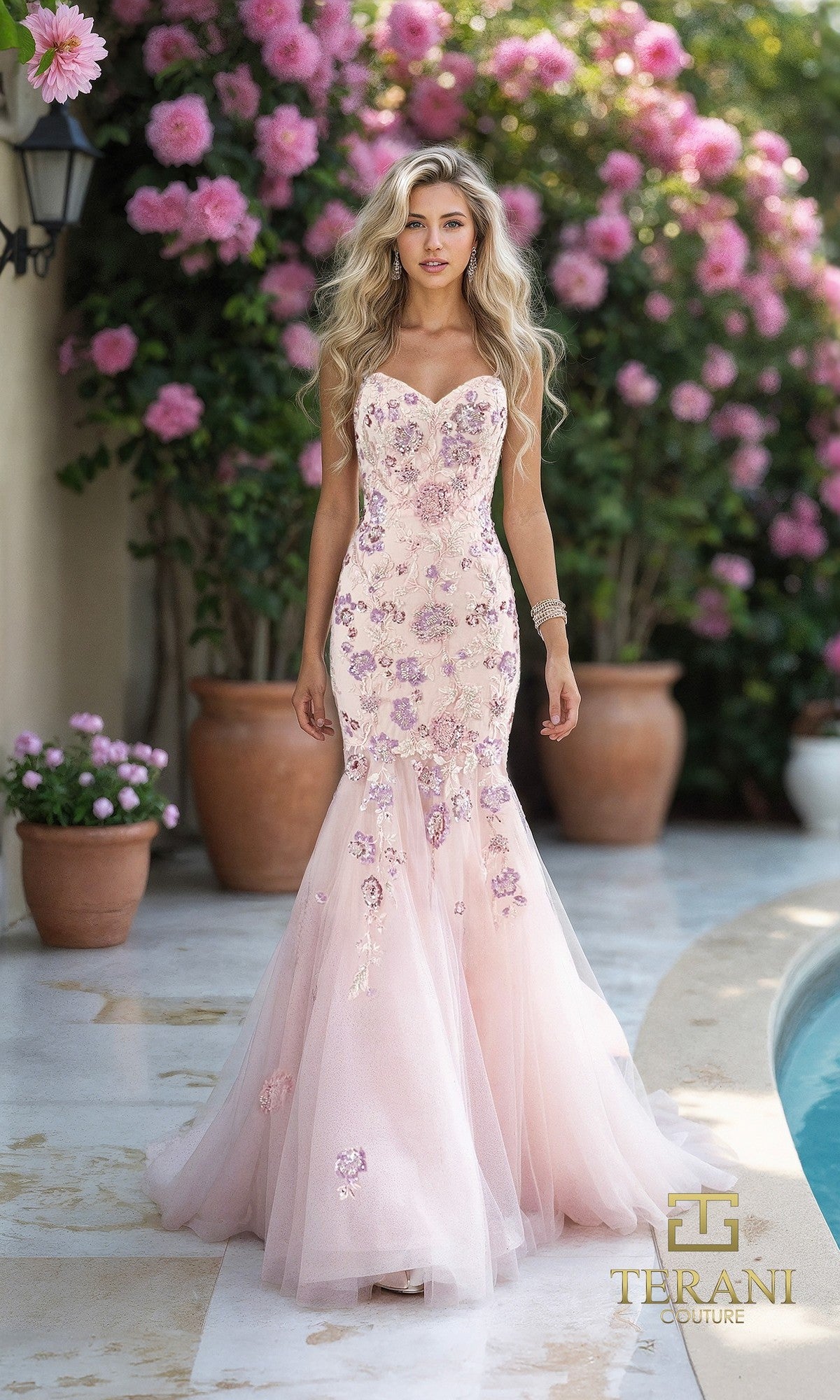 A woman wears the Terani 261P6193 long formal dress in blush—a strapless tulle mermaid gown with floral embellishments and delicate embroidery—standing by potted flowers outdoors. Terani Couture logo appears in the corner.