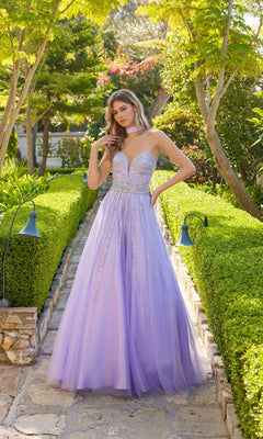 A woman in the Long Prom Dress: Juliet JT2620U—strapless, lavender tulle with a rhinestone-embellished bodice—stands on a stone garden path lined with hedges and greenery, gazing at the camera.