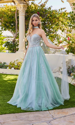 A woman stands outdoors wearing the Juliet JT2620U long prom dress in sage green, featuring a strapless, rhinestone-embellished bodice and a flowing tulle skirt.