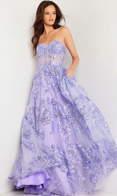 A woman wears the Jovani Strapless Lilac Long Prom Ball Gown 26223, featuring floral embroidery and a stunning lavender hue that adds elegance to her formal evening look against a white wall.