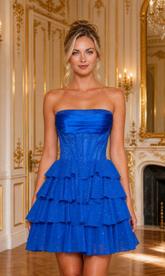 A woman poses in a gold-accented room wearing the Short Homecoming Dress: Poly USA 26244 in Royal, featuring a strapless corset bodice and layered skirt, with a chandelier and large mirror behind her.