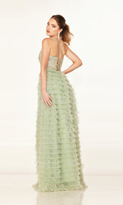 Woman in the Cecilia Couture 2624 long prom dress—light green, A-line with ruffled skirt, sheer corset bodice, and lace-up back—poses with one arm on her hip, looking over her shoulder.