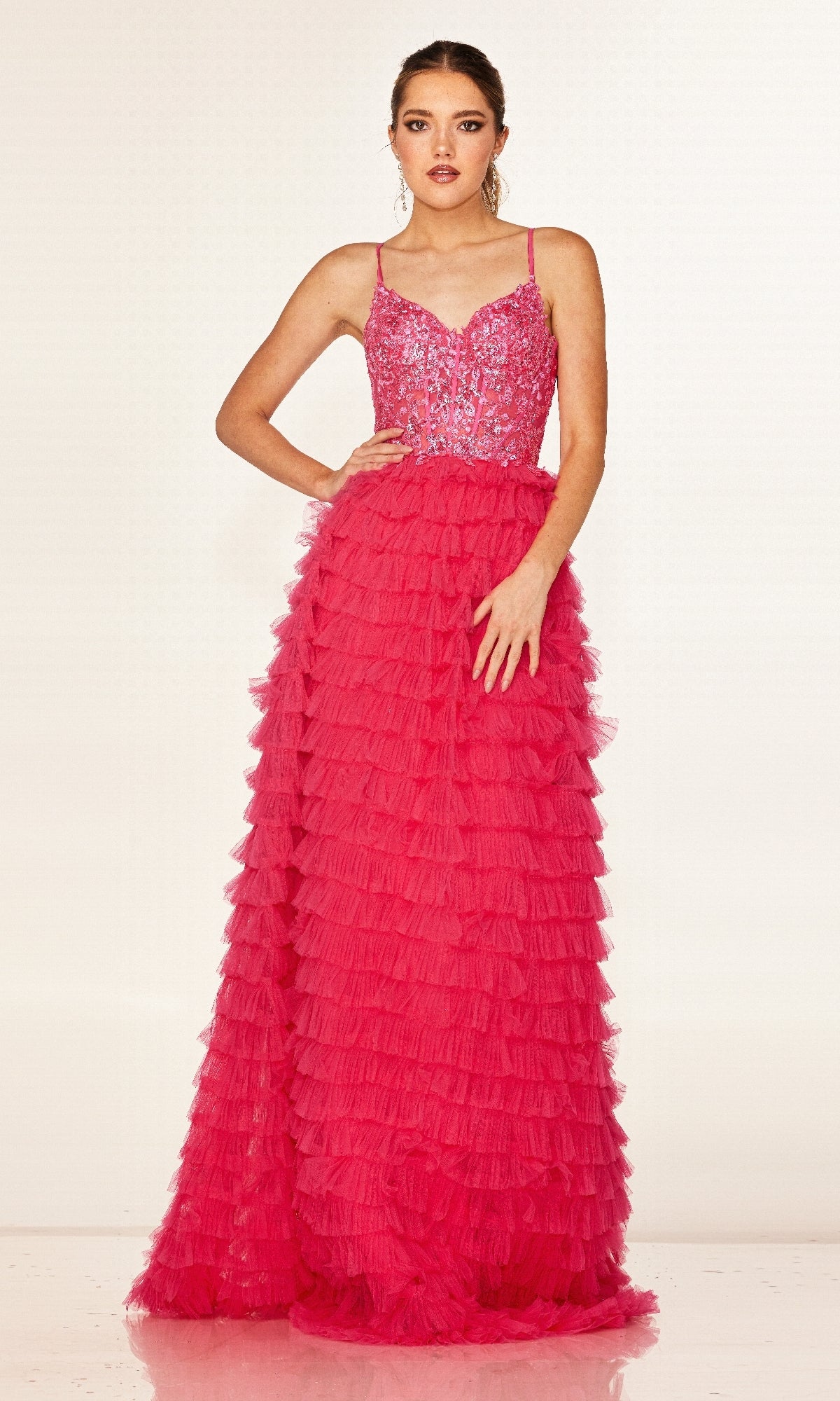 A woman stands against a plain light background in the Long Prom Dress: Cecilia Couture 2624, featuring a bright pink A-line silhouette with a fitted beaded bodice and a tiered ruffle skirt.