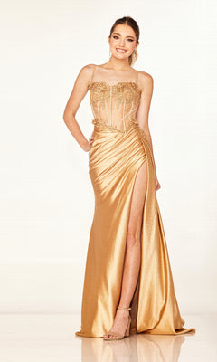 A woman wears the Cecilia Couture 2627 long prom dress in gold, featuring a sheer bodice, spaghetti straps, and a high leg slit, standing against a plain light background.
