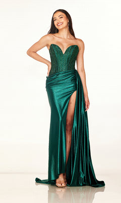 Wearing the Cecilia Couture 2629 long prom dress, a woman stands smiling with one hand on her hip, showcasing the form-fitting emerald green gown with its rhinestone corset bodice and high leg slit.