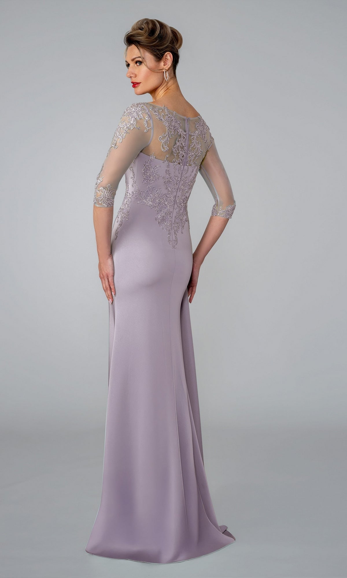 A woman wears a lavender Long Formal Dress: Stella Couture 26301, featuring intricate lace appliques on the bodice and shoulders with sheer three-quarter sleeves.