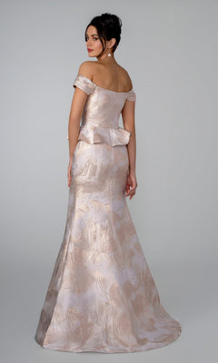A woman stands against a plain background wearing the Stella Couture 26305, an off-the-shoulder, floor-length light pink gown featuring a subtle pattern, sweetheart neckline, peplum detail, and a mermaid silhouette.