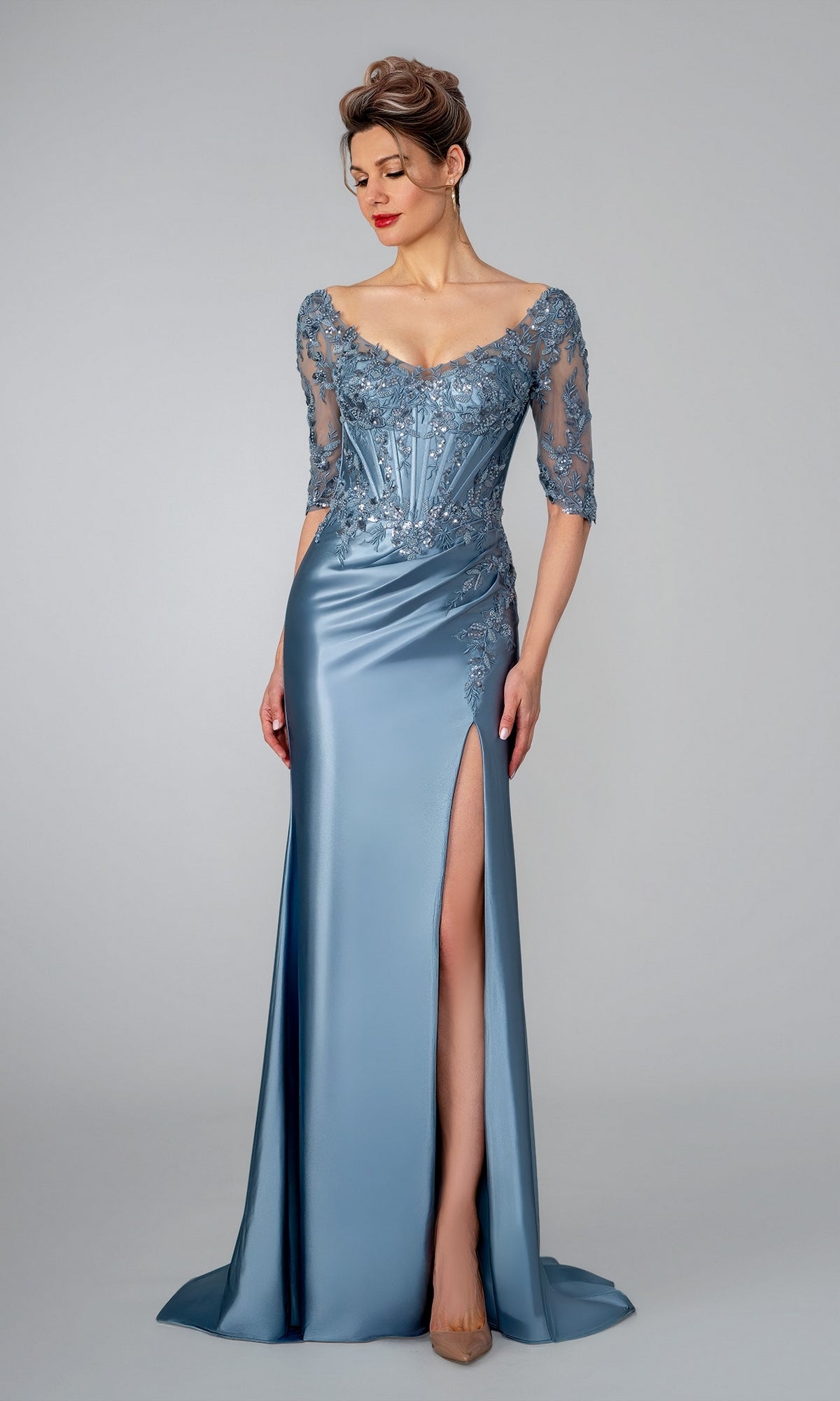 Stella Couture 26319 slate blue floor-length evening gown with a corset-style bodice, sheer lace sleeves, and a high leg slit.