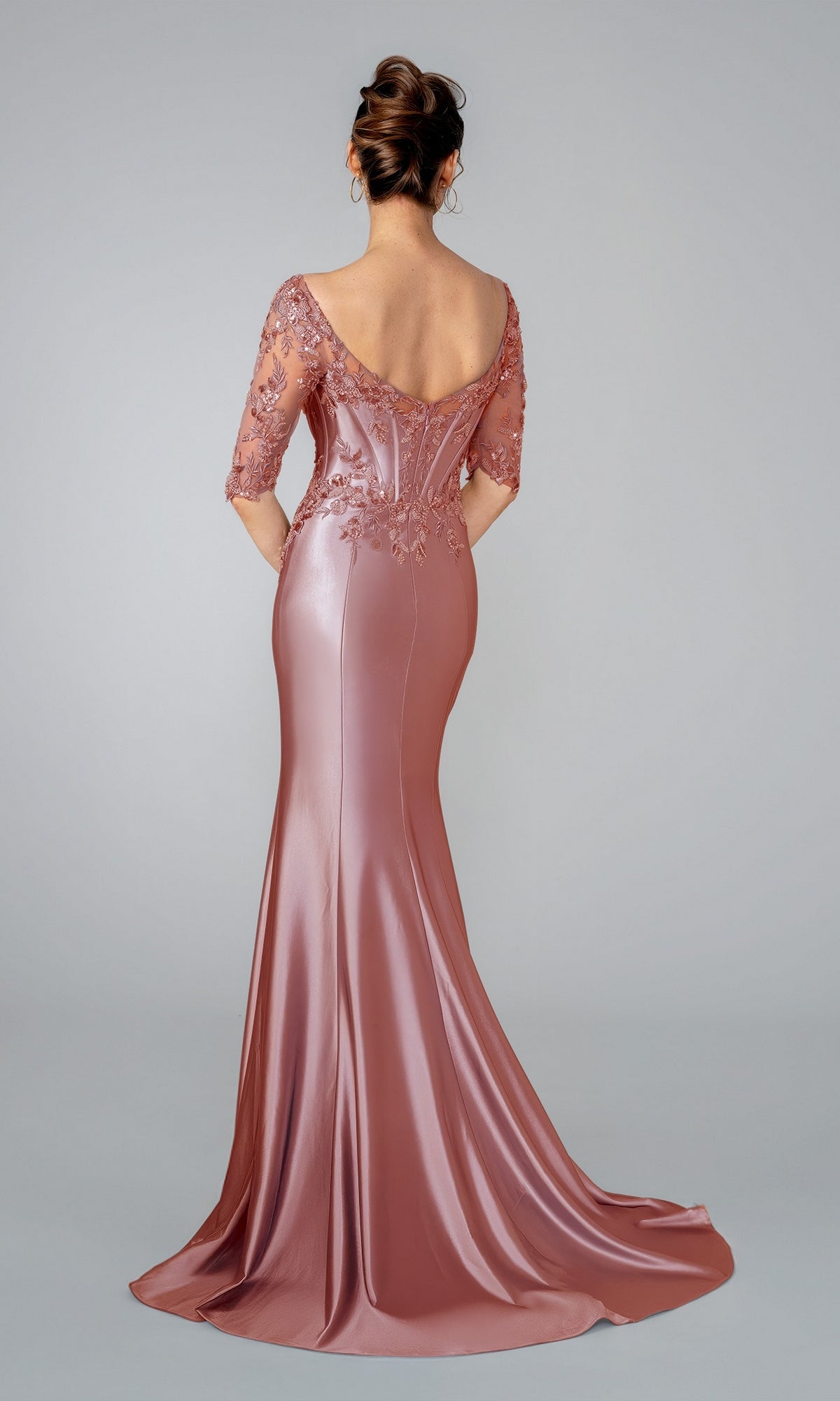 Back view of a rose-colored Stella Couture 26319 floor-length mermaid evening gown with a corset bodice and lace sleeve detailing.