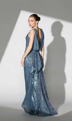 A woman in the Mac Duggal 26331 Cowl-Back Long Sequin Prom Dress faces away, looking over her shoulder as light casts her shadow on the wall.