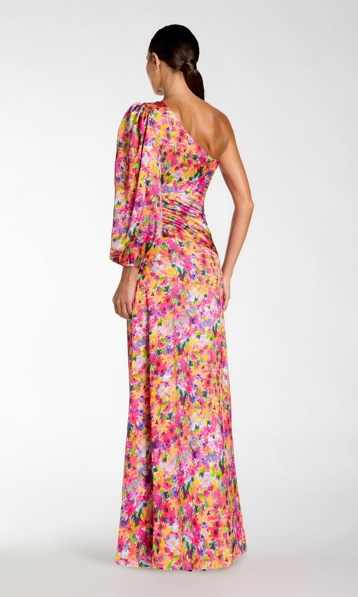 A woman faces away, wearing the Mac Duggal 2634 One-Sleeve Long Print Formal Dress with an asymmetrical neckline. Her hair is styled in a low ponytail, highlighting the dress’s elegant floral design.