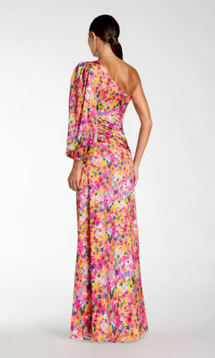 A woman faces away, wearing the Mac Duggal 2634 One-Sleeve Long Print Formal Dress with an asymmetrical neckline. Her hair is styled in a low ponytail, highlighting the dress’s elegant floral design.