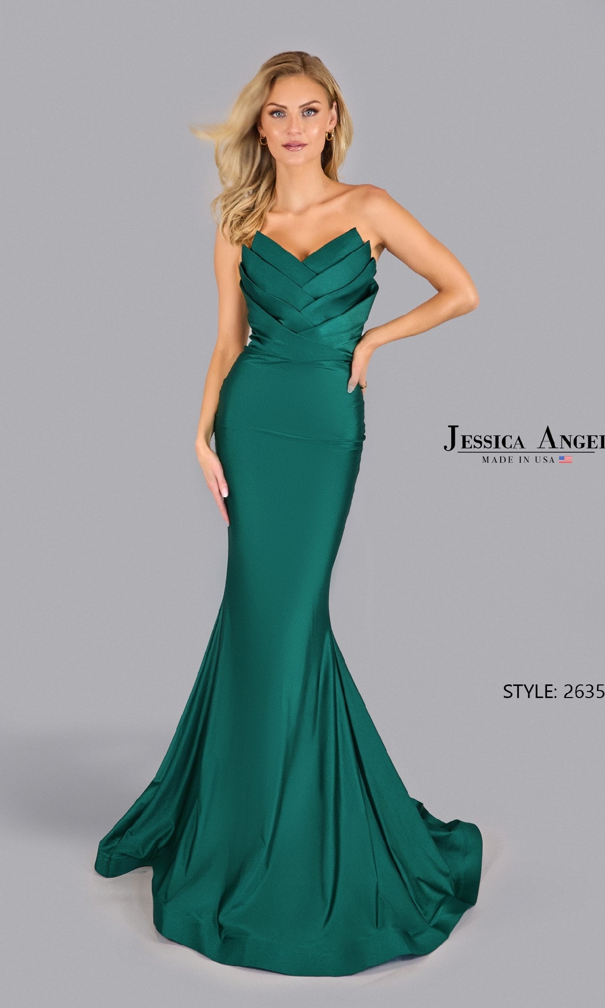 A woman models the Pleated Strapless Prom Gown: Jessica Angel 2635 in emerald green, standing poised against a plain gray background.