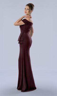 A woman wears a burgundy, off-the-shoulder Stella Couture 26371 evening gown with a peplum waist detail, perfect for a black-tie wedding.