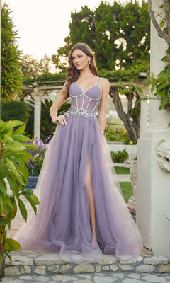 A woman stands outdoors in a lush garden wearing the Long Prom Dress: Juliet JT2638G in grey purple, featuring a corset bodice, sheer tulle skirt with silver embellishments, and a high slit.