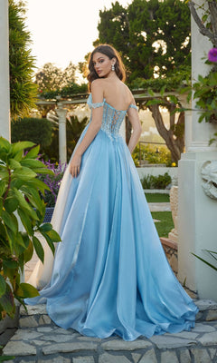 A woman in the Juliet JT2639G, a flowing light blue satin A-line prom dress with a corset bodice, stands outdoors on stone steps framed by greenery and columns.
