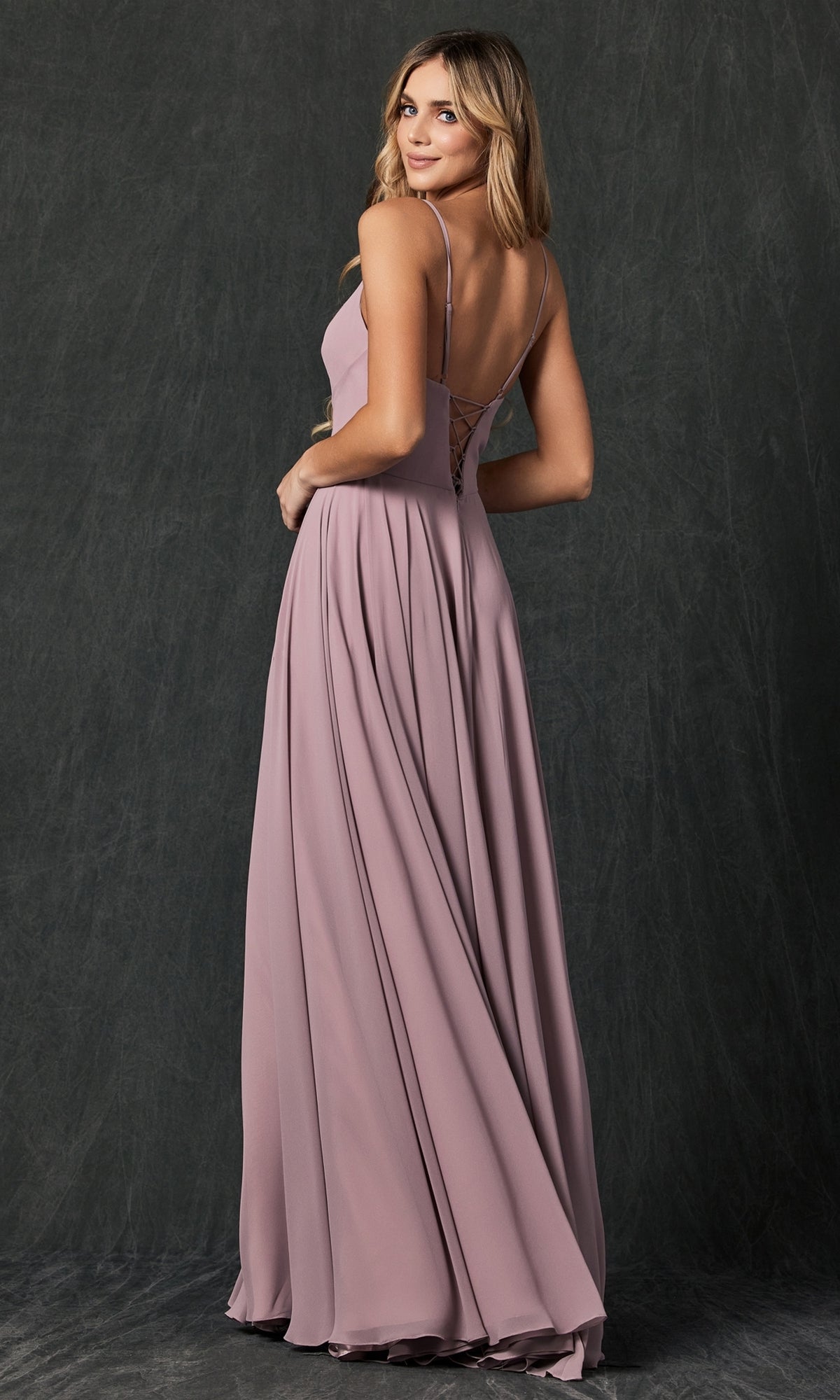 A woman in the Simple Long Formal Dress with Lace-Up Back 263, a sleeveless mauve gown, stands facing slightly away and looks over her shoulder against a dark textured background.
