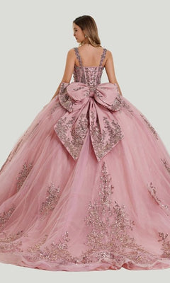 A woman wearing the Quinceanera Dress 26406 by Stella Couture—a pink ball gown adorned with silver embroidery, a large bow at the back, delicate embroidered mesh, and glitter tulle—stands against a simple light background.