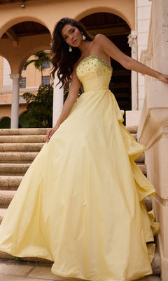 Woman in a Long Prom Dress (Ava Presley 26417) in soft yellow stands on stone steps, wearing a strapless ruffle ball gown with jeweled bodice, in front of an arched building.